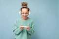 Beautiful positive smiling young woman wearing blue sweater isolated over blue background wearing white bluetooth