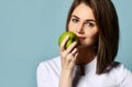 Beautiful positive woman dentist or doctor orthodontist in traditional white medical uniform holding green fresh apple near mouth