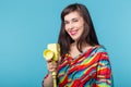 Beautiful positive young brunette woman holding in her hands a model of a yellow camcorder posing on a blue background Royalty Free Stock Photo