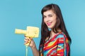 Beautiful positive young brunette woman holding in her hands a model of a yellow camcorder posing on a blue background Royalty Free Stock Photo