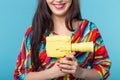 Beautiful positive young brunette woman holding in her hands a model of a yellow camcorder posing on a blue background Royalty Free Stock Photo