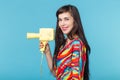 Beautiful positive young brunette woman holding in her hands a model of a yellow camcorder posing on a blue background Royalty Free Stock Photo