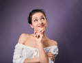 Beautiful positive young casual woman with hand under the face thinking and looking up in white shirt on purple background Royalty Free Stock Photo