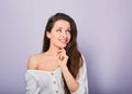 Beautiful positive young casual woman with hand under the face thinking and looking up in white shirt on purple background Royalty Free Stock Photo