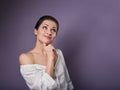 Beautiful positive young happy woman with hand under the face thinking and looking up in casual shirt on purple background Royalty Free Stock Photo