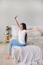 Beautiful pre-teen girl in casual clothes do stretching exercises seated on bed in cozy bedroom in the morning Royalty Free Stock Photo