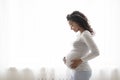 Beautiful pregnant black woman hugging tummy while standing near window at home Royalty Free Stock Photo