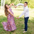 Beautiful pregnant couple happy together expecting a child. Man and woman walking in the park showing heart with hands. Share the Royalty Free Stock Photo