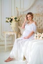 Beautiful pregnant girl in a home clothes sitting in the interior on a bed of roses