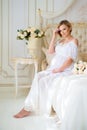 Beautiful pregnant girl in a home clothes sitting in the interior on a bed of roses