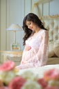 Beautiful pregnant girl in a lace negligee sitting on a bed of roses Royalty Free Stock Photo