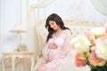 Beautiful pregnant girl in a lace negligee sitting on a bed of roses Royalty Free Stock Photo