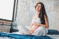 Beautiful pregnant girl young woman with long curly hair sitting in lotus pose on bed. Pregnancy yoga and nature ethnic beauty Royalty Free Stock Photo