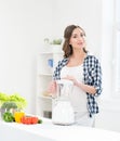 Beautiful pregnant smiling woman cooking with a blender