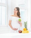 Beautiful pregnant smiling woman in the kitchen eating fruits