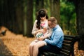 Beautiful pregnant stylish couple relaxing outside in the autumn park sitting on bench.