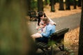 Beautiful pregnant stylish couple relaxing outside in the autumn park sitting on bench.