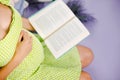 Beautiful pregnant woman dressed in green dress reads a book while sitting on a bed at home with a purple background. Royalty Free Stock Photo