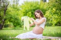 Beautiful pregnant woman holding baby bodysuit and smiling in the park Royalty Free Stock Photo