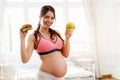 Beautiful pregnant woman holding a burger and an apple