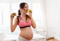 Beautiful pregnant woman holding a burger and an apple