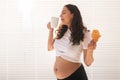 Beautiful pregnant woman holding croissant and cup of coffee in her hands during morning breakfast. Concept of good Royalty Free Stock Photo