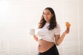 Beautiful pregnant woman holding croissant and cup of coffee in her hands during morning breakfast. Concept of good Royalty Free Stock Photo