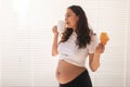 Beautiful pregnant woman holding croissant and cup of coffee in her hands during morning breakfast. Concept of good Royalty Free Stock Photo