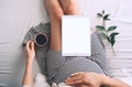 Beautiful pregnant woman holding her belly and relaxing with cup of coffee and digital tablet during pregnancy. Young mother