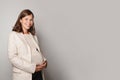 Beautiful pregnant woman hugging her tummy, smiling and standing against grey studio wall background Royalty Free Stock Photo