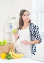 Beautiful pregnant woman in the kitchen with shopping bag and apple Royalty Free Stock Photo