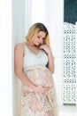 A beautiful pregnant woman in beautiful lace dress stands near a bright window. Feminine sexuality, femininity and beautiful Royalty Free Stock Photo