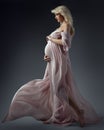 Beautiful Pregnant Woman looking at Belly in Waving Dress Side view. Happy Mother Profile Portrait embracing Abdomen in Pink Gown Royalty Free Stock Photo