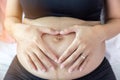 Beautiful pregnant woman make symbol of love and touching on her belly. Pregnant girl has the first child of family. She love her Royalty Free Stock Photo