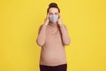 Beautiful pregnant woman in medical face mask keeping fingers on temples, suffering from headache, being scared to get infected of