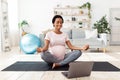 Beautiful pregnant woman meditating to online video on laptop computer at home Royalty Free Stock Photo