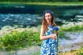 Beautiful pregnant woman mother to be in wreath and blue dress standing in front of scenic river in sunset time in summer. Royalty Free Stock Photo