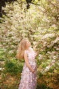 Beautiful pregnant woman in pink lace dress touching belly and smelling flowers on the tree Royalty Free Stock Photo