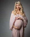 Beautiful Pregnant Woman Portrait in Pink Chiffon Dress over Gray. Happy Mother with Curly Long Hair and Makeup in Silk Gown. Royalty Free Stock Photo