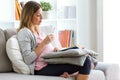 Beautiful pregnant woman reading a book and eating yogurt on the sofa at home. Royalty Free Stock Photo