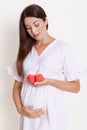 Beautiful pregnant woman with red baby shoes isolated on white background, lady expecting baby looking at small booties in her Royalty Free Stock Photo