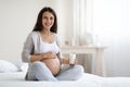 Beautiful pregnant woman sitting on bed, holding glass of milk Royalty Free Stock Photo