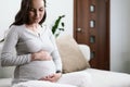 Beautiful pregnant woman sitting on couch with hands on pregnant belly, happy pregnancy Royalty Free Stock Photo
