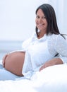 Beautiful pregnant woman sitting at sofa and keeping hand on belly. Royalty Free Stock Photo