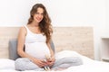 Beautiful pregnant woman sitting on the sofa, smiling and holding a toy in your arms.