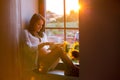 Beautiful pregnant woman, sitting on window shield, reading from Royalty Free Stock Photo