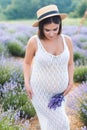 beautiful pregnant woman standing in white dress in violet lavender field and holding small bouquet Royalty Free Stock Photo