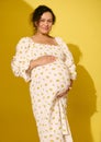 Beautiful pregnant woman in sundress, gently caresses her belly, smiles looking at camera, isolated on yellow background Royalty Free Stock Photo