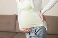 Beautiful pregnant woman touching her tummy and keeping one hand on her back at home on sofa Royalty Free Stock Photo