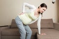 Beautiful pregnant woman touching her tummy and keeping one hand on her back at home on sofa Royalty Free Stock Photo